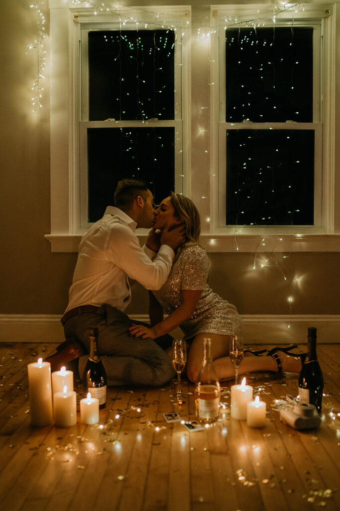 Couple kissing on the floor beneath string lights and candles, an intimate nighttime moment photographed by a low-light New England wedding photographer.