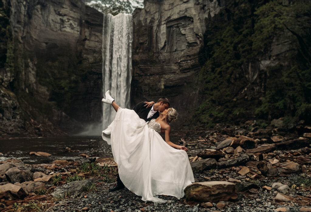 The groom dips the bride in front of a dramatic waterfall, capturing a cinematic moment inspired by adventurous outdoor wedding venues New England offers.