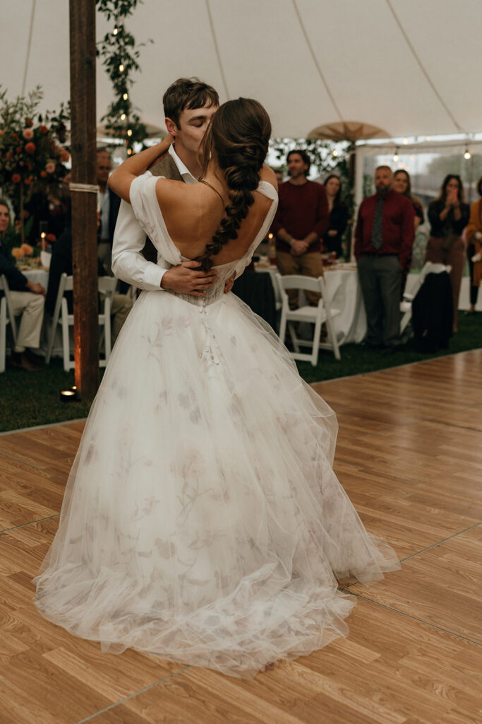 Newlyweds share a kiss on the dance floor as guests gather around them, a candid moment from an intimate New Hampshire wedding weekend.