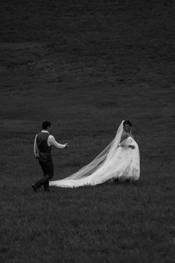 Bride crossing an open field while the groom follows, creating a dramatic black-and-white portrait by a cinematic wedding photographer in New England.