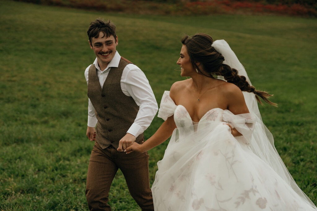The couple walks hand in hand, smiling at each other with effortless joy, styled in a relaxed yet refined look that reflects the atmosphere of elegant New England castle-inspired wedding settings.