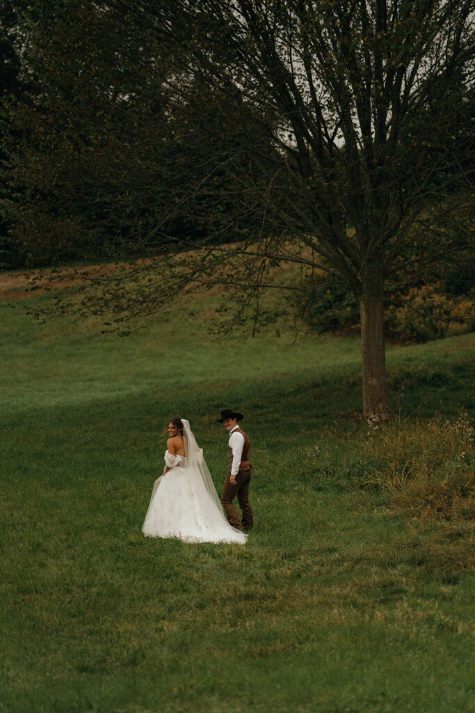 Couple standing together in a secluded grassy landscape framed by trees and soft evening light during a romantic elopement in New England.