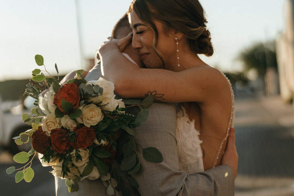 Bride embracing a loved one while holding a bouquet of white and rust-colored flowers, an emotional detail often valued by a New England wedding photographer.
