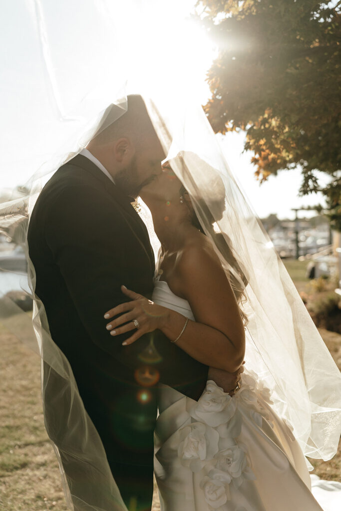 Cinematic Wedding Photographer Rhode Island | Aisha Lee Photography Cinematic Wedding Photographer | A bride and groom share a kiss under a flowing veil, backlit by the sun.