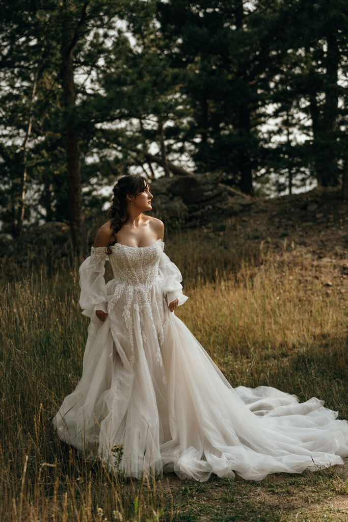 Unique Wedding Venues New England | Aisha Lee Photography Cinematic Wedding Photographer | A woman in a flowing, off-shoulder white wedding gown stands in a forest. Sunlight filters through the trees, creating a serene, enchanting atmosphere.