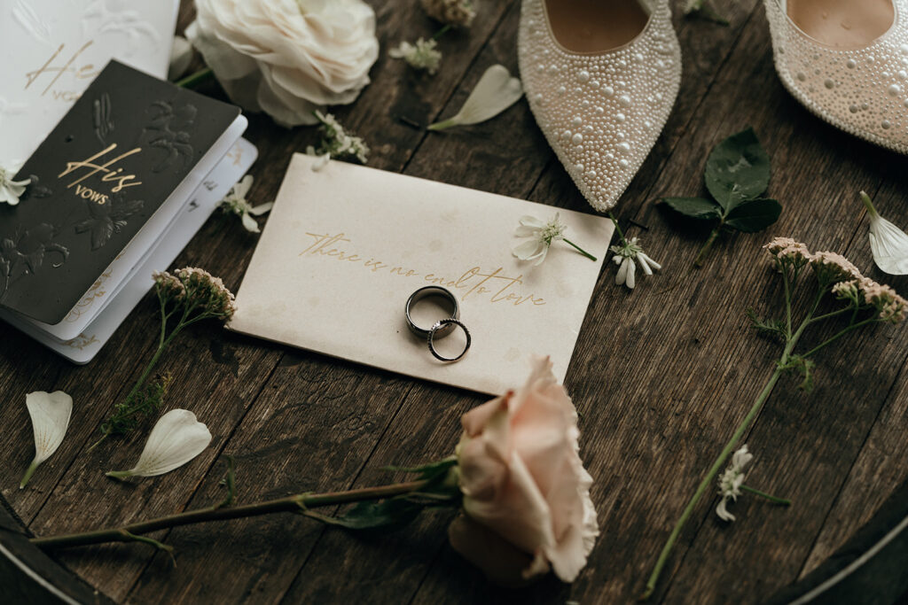 Wedding rings rest on a handwritten note beside a jeweled shoe and pale rose on a wooden surface. A thoughtful flat lay for castle wedding venues New England couples love.