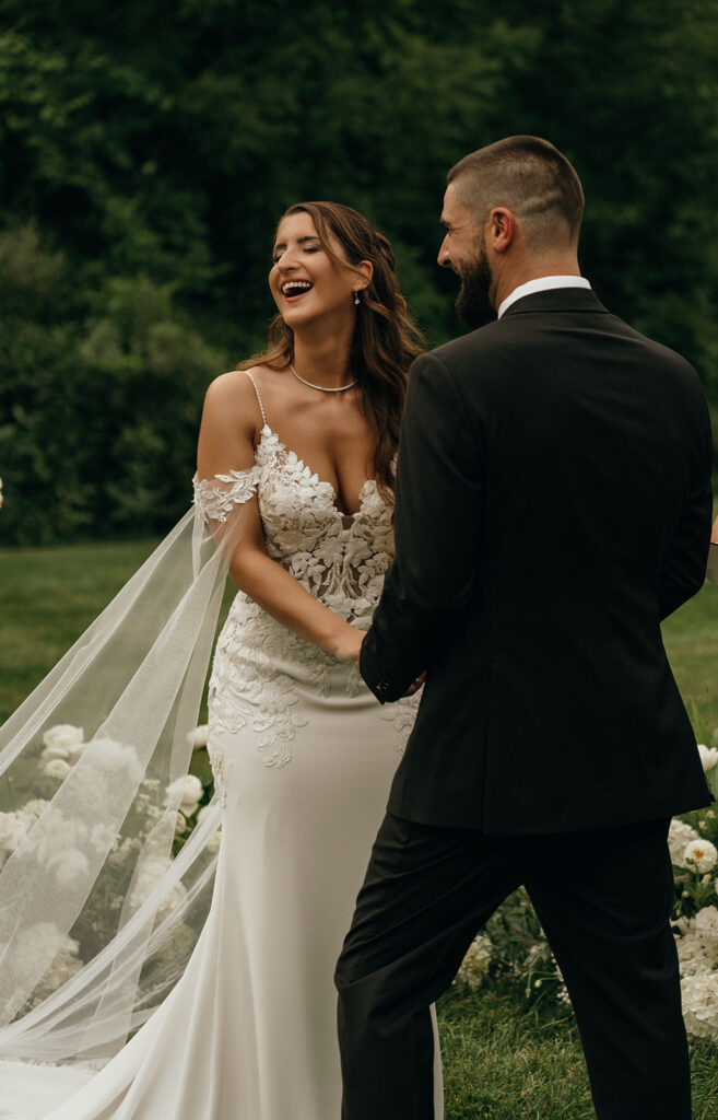 The couple laughs together during their ceremony, her veil drifting behind her as they hold hands in a setting that reflects the charm of New England castle wedding venues.