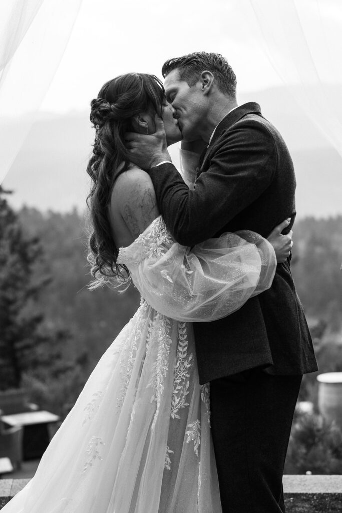 Black-and-white documentary wedding photograph of a bride and groom kissing beneath her veil