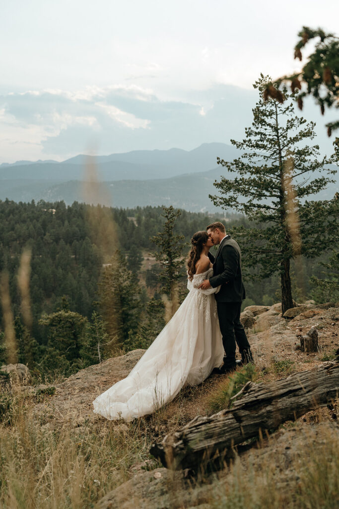 Adventure Wedding and Elopement Photographer New England | Aisha Lee Photography Cinematic Wedding Photographer | A bride and groom embrace on a grassy mountain overlook, surrounded by trees under a cloudy sky