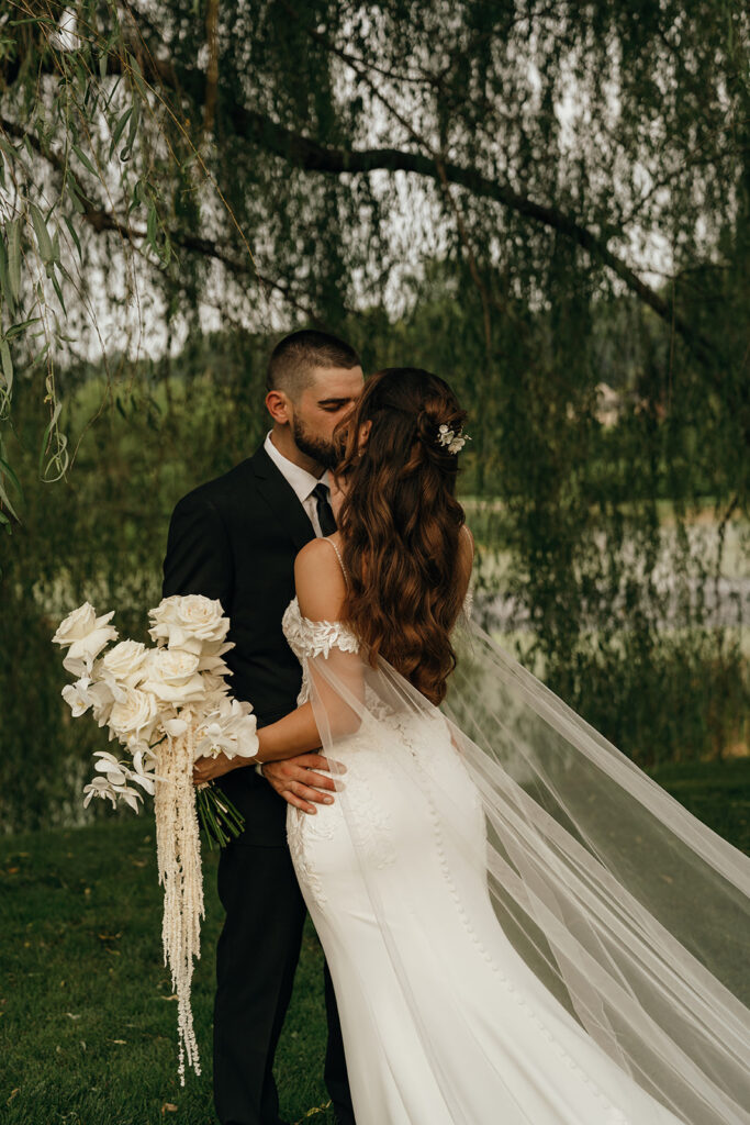 Bride and groom embracing beneath willow branches beside the water during a quiet portrait session inspired by coastal New England weddings.