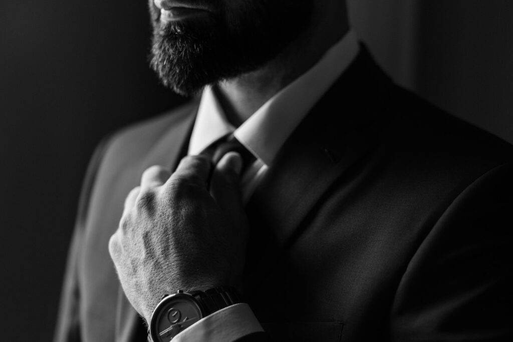 Close-up black-and-white portrait of a groom adjusting his tie, bringing a timeless editorial detail to New Hampshire wedding photography.