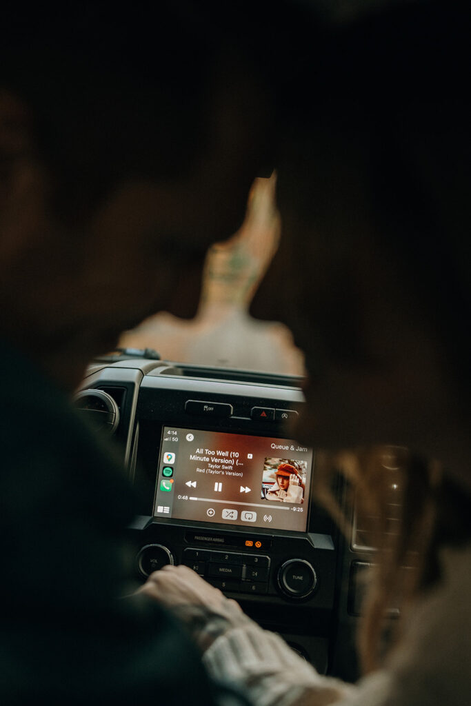 Traveling Cinematic Wedding and Elopement Photographer | Aisha Lee Photography Cinematic Wedding Photographer | Blurred couple faces surrounding a car dashboard displaying music, conveying warmth and intimacy. Song playing on a digital screen.