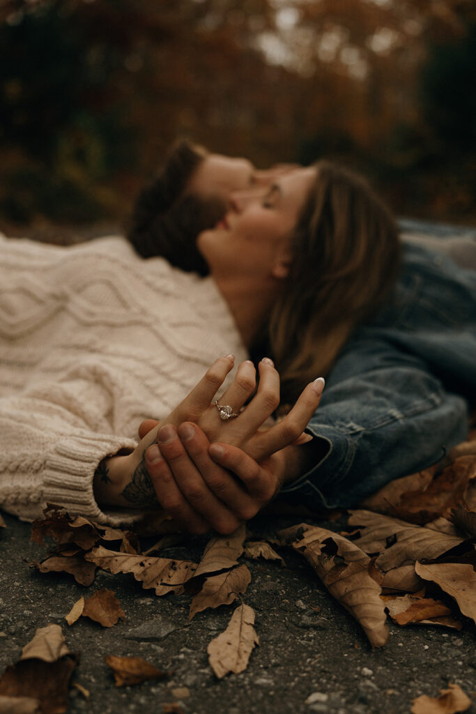 Destination Wedding and Elopement Photographer | Aisha Lee Photography Cinematic Wedding Photographer | A couple lies on the ground among autumn leaves, holding hands