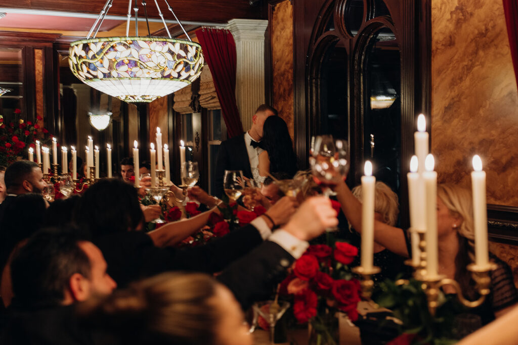Newlyweds kissing during a candlelit wedding reception as guests raise their glasses in celebration