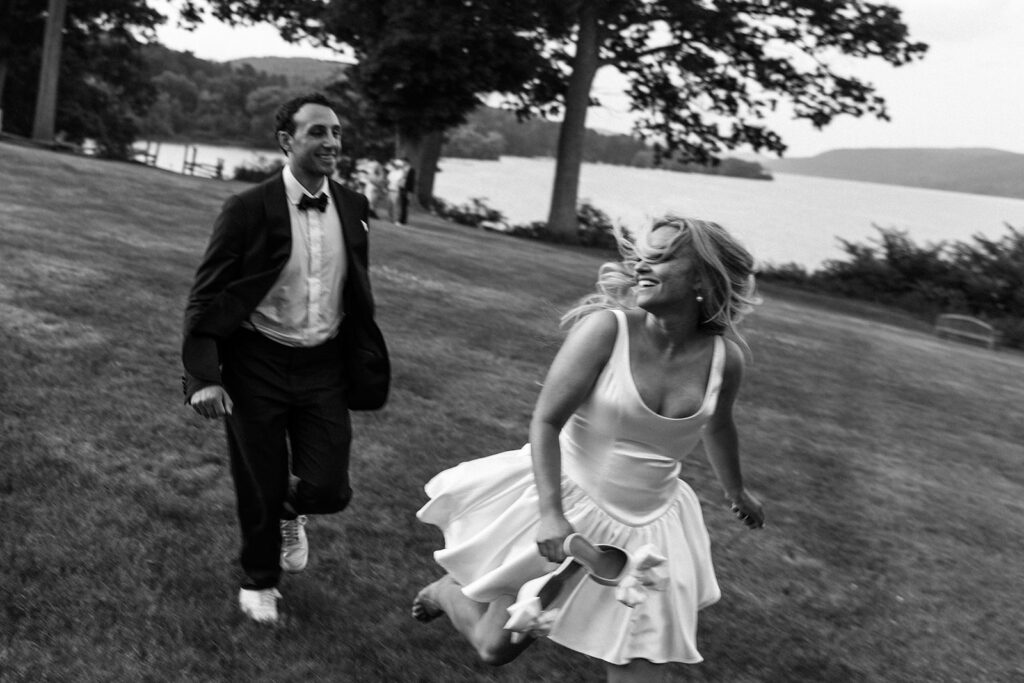 Bride running across the lawn laughing with guests near the waterfront during a candid reception moment at a New England coastal wedding venue.