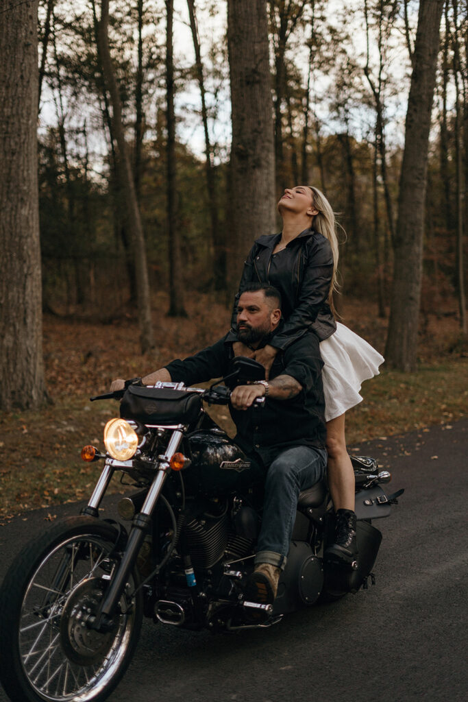 Eloping in New England | Aisha Lee Photography Cinematic Wedding Photographer | A man rides a motorcycle down a forest road while a woman sits behind him, head tilted back, enjoying the ride. The scene feels adventurous and free.
